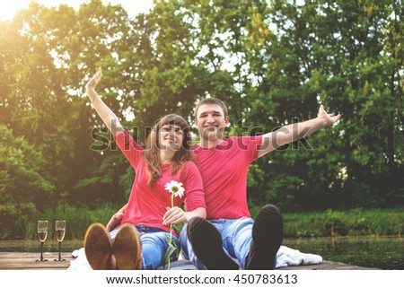 Cheerful pair young people in red shirts siyat by the river on a wooden bridge. A girl holding a white daisy. Toning