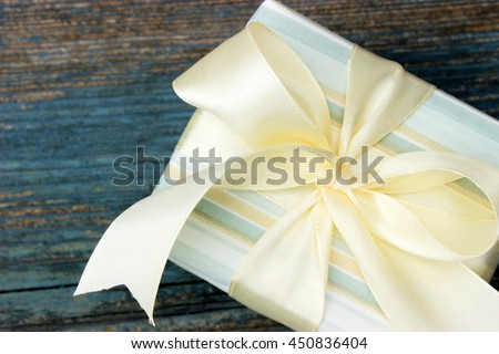 Cute blue gift box decorated with white satin ribbon and bow on old wooden background. Concept for greeting theme
