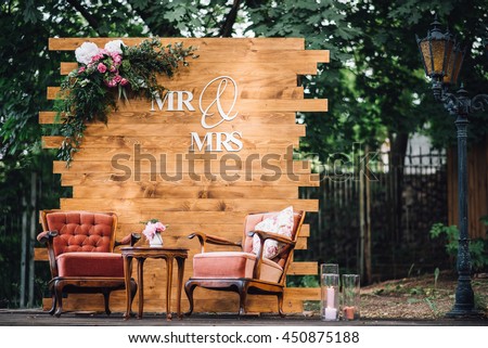 Wedding. Banquet. Mr. & Mrs. signs on wooden board decorated by flowers and greenery and lounge zone including chairs and tables. Royalty-Free Stock Photo #450875188