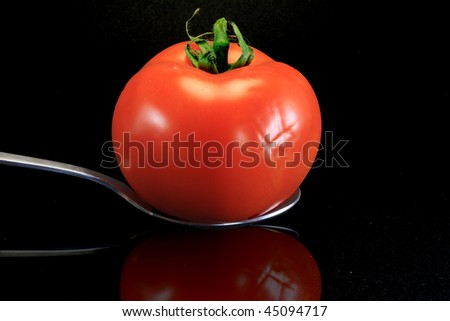tomato in spoon isolated on black