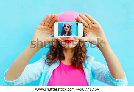 Woman makes self-portrait on smartphone view screen over colorful blue background