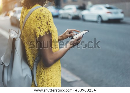 Young hipster girl in yellow dress traveling in Europe and using an app for search local cafe or sightseeing, female hands typing on touch screen of cellphone device to send an sms message