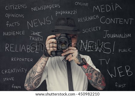Bearded dslr photographer with tattooes on his arms over school desk background.