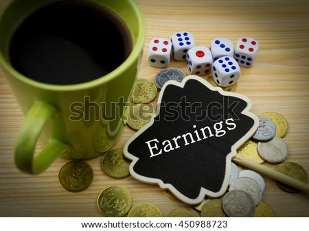 Financial concept : Note with written word earnings (Coins,dices and coffee on wooden background)