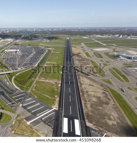Aerial view of a runway at Schiphol Amsterdam Airport with the city on the clear blue horizon. The runway looks like a highway.