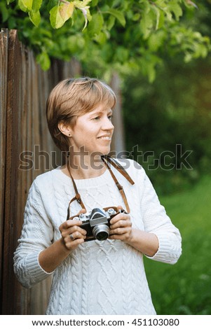 Girl in a white sweater with retro photo camera near the wooden fence outdoors