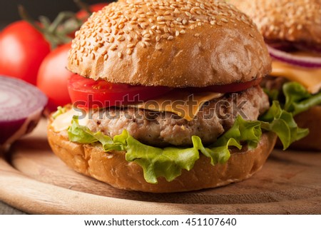 Close-up photo of home made hamburger of beef, onion, tomato, lettuce, cheese and spices with a glass of light beer. Fresh burger closeup on wooden rustic table with potato fries and chips.