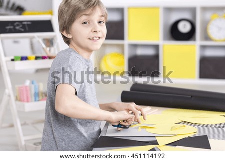 Smiling young boy in an art studio cutting of the paper colorful collage for art classes at school