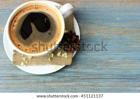 Cup of sweet tasty coffee decorated with grey linen napkin, dry petals of white flowers and natural linen cone on old vintage wooden background. Copy space