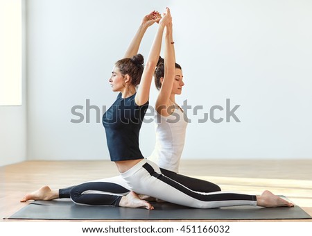 Two young women doing yoga asana Eka Pada Rajakapotasana. One legged king pigeon. Partner yoga