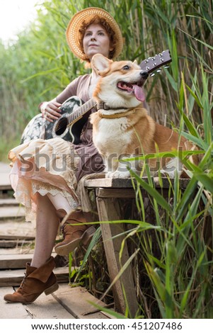 redhead woman with guitar and corgi dog in countryside