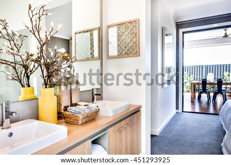 Modern washroom with fancy flower vase next to the silver faucet and sink near perfume bottles on the wooden counter top and the hallway to an outside patio area with chairs and tables