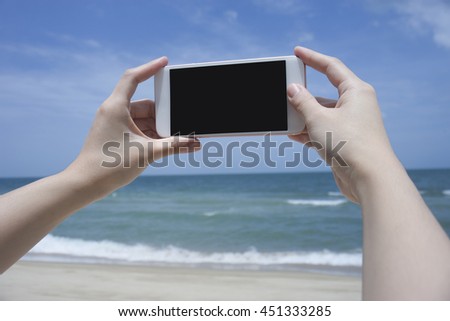 Close up of woman's hand holding smart phone, mobile, smart phone over blurred beautiful blue sea to take a photo of the sea,phone with black screen