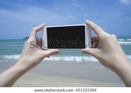 Close up of woman's hand holding smart phone, mobile, smart phone over blurred beautiful blue sea to take a photo of the sea,phone with black screen

