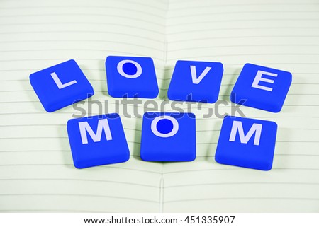 Close up Blue Scrabble Letter Tiles for word LOVE MOM on book page