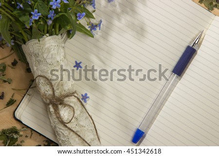 Spring bouquet of forget-me colors in the morning rays of the sun, notebook and pen on the wooden table