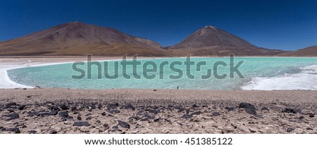 Nice view of the lagoon with aquamarine water from the mountain, mountains in the background, black stones in the foreground and small person standing on the edge, Laguna Verde, Bolivia, South America