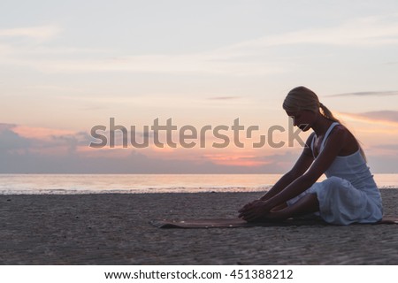 Young woman doing yoga at the beach at sunset