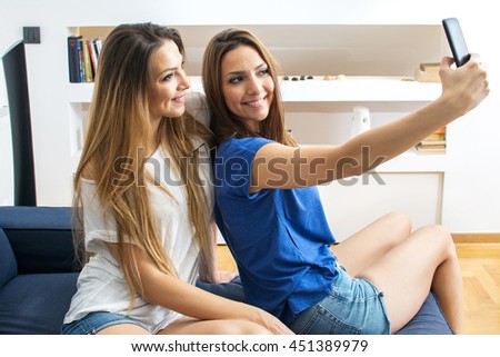 Young twin sisters on the couch taking a selfie with smartphone at home in the living room.