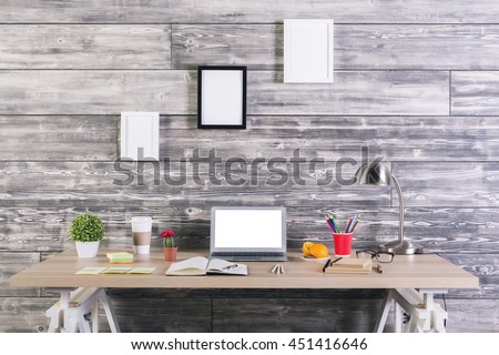 Modern designer desktop with blank white laptop, picture frames above, plants, stationery and other items. Mock up