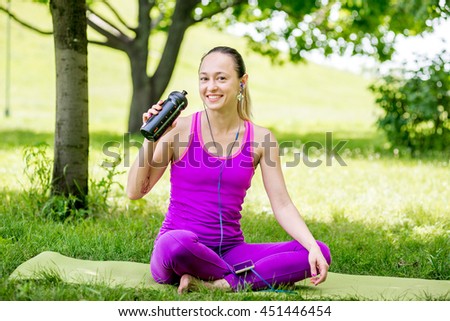 Woman sitting at the grass and drinking water after workout