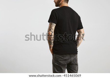 Brutal attractive bearded biker man with tattooed hands poses backside in black blank t-shirt from premium thin cotton, isolated on white mockup Royalty-Free Stock Photo #451465069