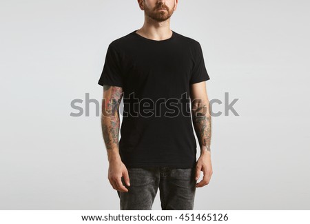 Brutal attractive bearded biker man with tattooed hands poses in black blank t-shirt from premium thin cotton, isolated on white mockup Royalty-Free Stock Photo #451465126