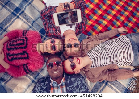 Toned. People in sunglasses lying on picnic rug and smiling for camera. Closeup picture of best friends making selfie on mobile or smart phone on picnic.