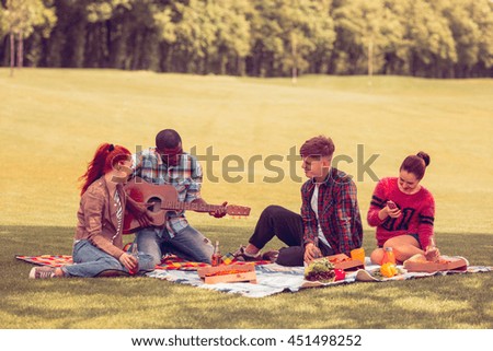 Toned. Picture of best friends spending free time on picnic. Two men and two women communicating or talking and listening to guitar. Picnic concept.