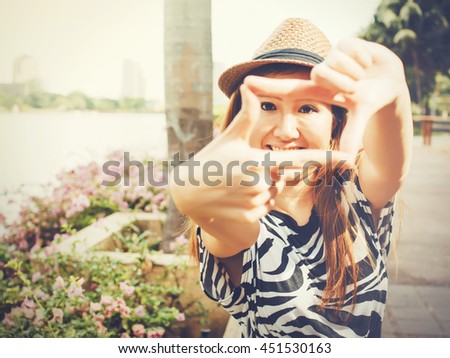 Beautiful Asian girl using hands framing for taking photos in outdoor scene in Vintage tone