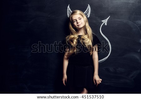 Funny little imp girl. Cute child girl posing with imp horns and tail drawn on a blackboard.