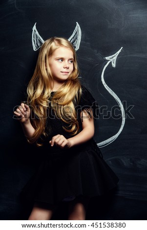 Funny little imp girl. Cute child girl posing with imp horns and tail drawn on a blackboard.