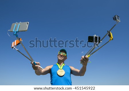 Gold medal athlete smiling for his many gadgets on selfie sticks as he poses for a picture