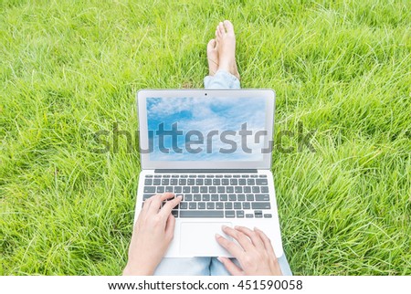 Asian woman sitting on grass floor in the garden textured background for use a notebook computer with blue sky in screen of notebook
