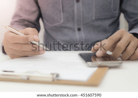 Concept Document sign off - Smart businessman signing document with searching information from smart phone.