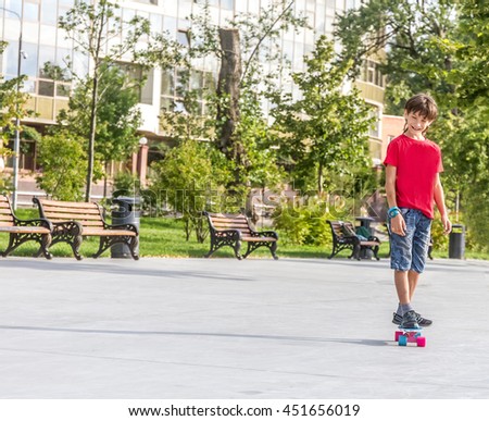 outdoor portrait of young smiling teenager boy riding short modern cruiser skateboard, urban background