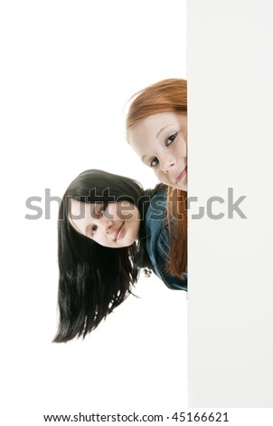 Two cute teenage girls behind a blank sign with room for copy