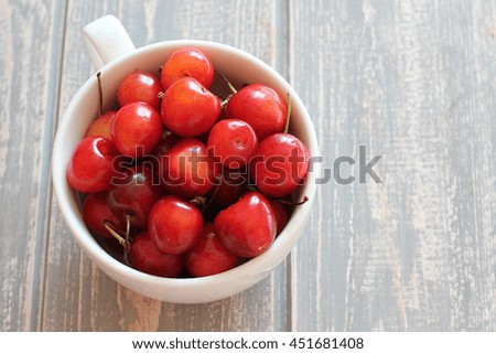 Cherries in white cup on wooden grey desk. Stock photo.