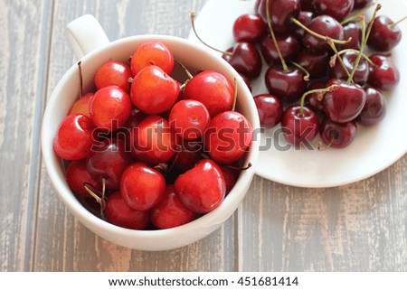 Cherries in white cup on wooden grey desk. Stock photo.
