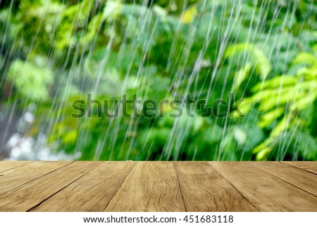 Empty wooden table on green trees in rainy nature background