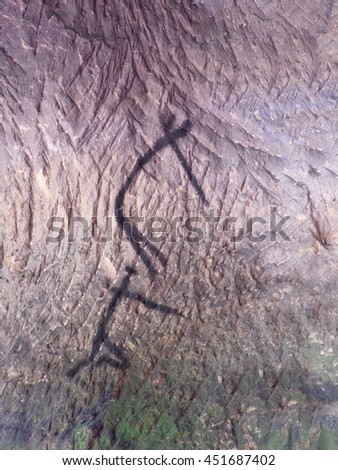 Abstract children art in sandstone cave. Black carbon paint of human hunting on sandstone wall, copy of prehistoric picture.