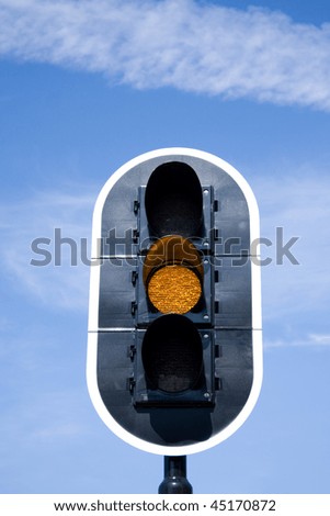 Picture of a traffic light that turned to amber with a blue sky on the background.
