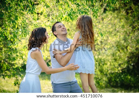 Young happy family three father catch his daughter and hug her near mother in the park