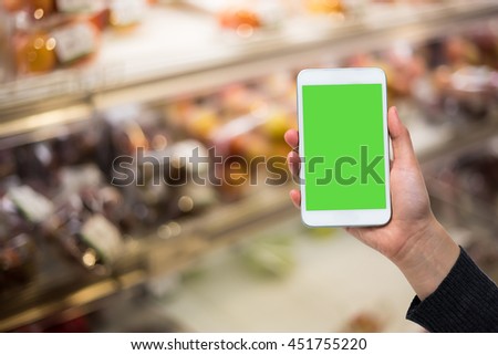 Holding phone with green screen on burred supermarket 