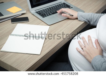 Pregnant woman with notebook to working the business at the table in office, New Mom's pregnancy and baby health care concept
