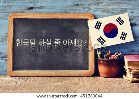 a chalkboard with the question do you speak Korean? written in Korean, a pot with pencils, some books and the flag of South Korea, on a wooden desk