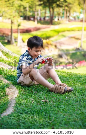 Happy asian boy with camera on nature background. Child relaxing outdoors in the day time at park, travel on vacation. Positive human emotion.