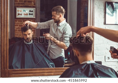 Young handsome barber making haircut of attractive man in barbershop Royalty-Free Stock Photo #451865992