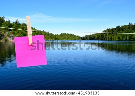 blank pink sticky note hanging on a clothes line with a lake in the background.