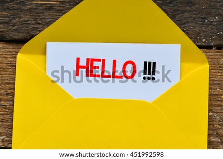 Message hello on a white sheet in a yellow envelope on a wooden background.